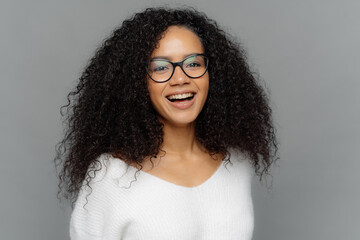 Candid shot of optimistic curly woman laughs positively, being in good mood, has healthy skin,...