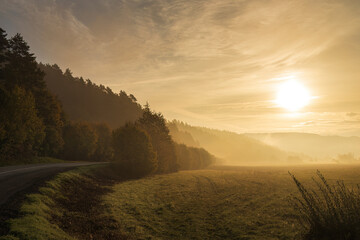 A bend of the road at the morning light of a foggy autumn landscape.