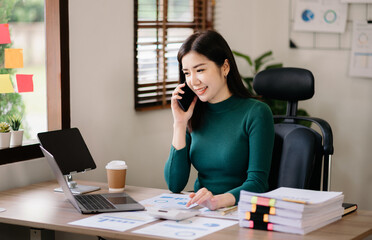 Business asian woman Talking on the phone and using a laptop with a smile while sitting at office.