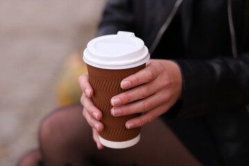 Close-up of female hands holding a large plastic disposable cup with coffee, cappuccino