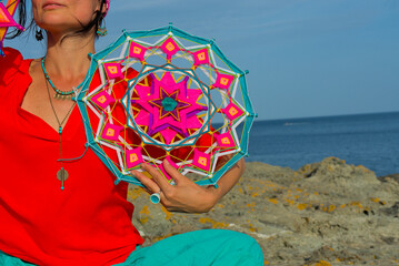 A woman holds in her hands a mandala made of multi-colored threads. Boho style clothes. On the...
