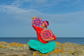 A woman holds in her hands a mandala made of multi-colored threads. Boho style clothes. On the...