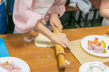 Young girl rolls out piece of dough with rolling pin to create pizza dough. Training (master class) in culinary arts.