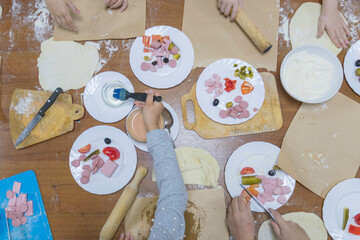 White plates with set of pizza ingredients and kitchen utensils stand on wooden table. Children's hands create. Cooking master class for children.