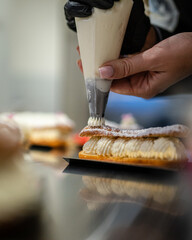 Une pâtissière prépare un éclair à la crème dans une pâtisserie  - obrazy, fototapety, plakaty