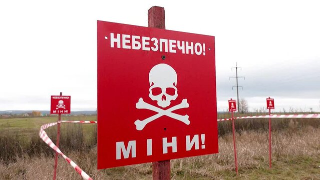 Red warning signs with the inscription Danger Mined and enclosing tapes in the middle of the field. Russian-Ukrainian war 2022. The Russian army mined the territory of Ukraine. Mines and grenade