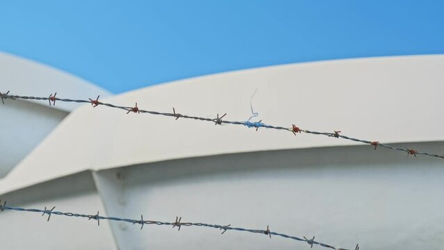 Rusty Barbed Wire with String of Nylon Material Moving in the Wind