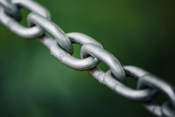 Closeup to a stainless shiny chain links against green backdrop