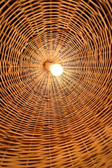 Light bulb glowing in the middle of a wicker lamp