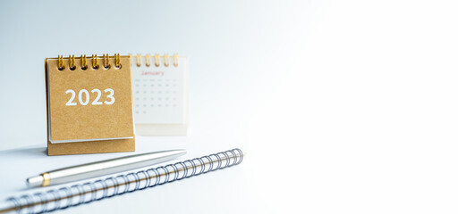 Happy new year 2023 banner background. 2023 numbers year on small beige desk calendar cover on notepad with pen on white background with copy space, to do list concept.
