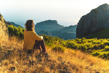 Woman sitting on a mountain meadow enjoying the beautiful mountain landscape of Pico do Ariero at...