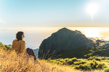 Woman sitting on a mountain meadow enjoying the beautiful mountain landscape of Pico do Ariero at...
