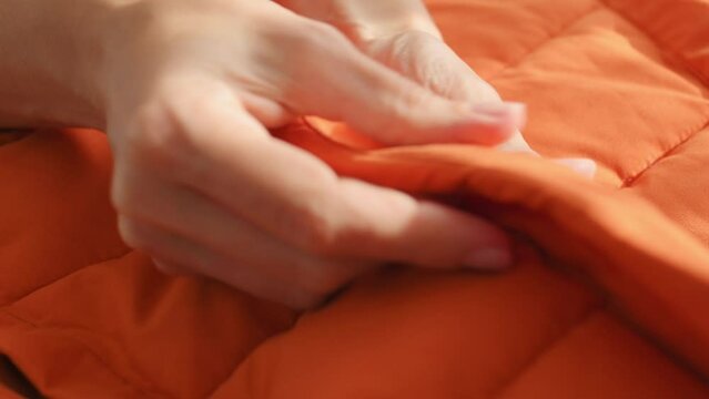 Female hands touching groping material orange waterproof fabric of winter jacket, down jacket. Textile, clothing production, autumn bright jacket. Fashion, Style. Clothes background