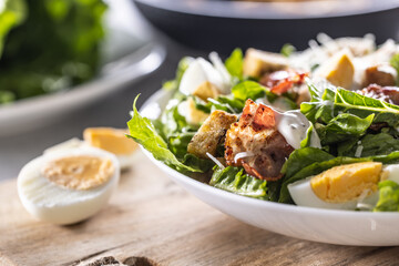 A white bowl full of Cezar salad with croutons, bacon and parmesan cheese