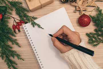 Woman writing New Year resolution or Christmas wishlist in notebook,hands close-up,top view.New Year and Christmas concept.Planning concept.