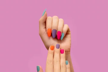 Poster Female hands with colorful nail design. Glitter nail polish manicure: purple, green, pink and orange on pink background © devmarya