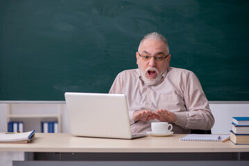 Old male teacher drinking coffee in the classroom