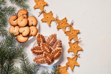 Festive Christmas cookies on plates with star garland anf fir tree branches. Shortbread cookies on a white background. Copy space.
