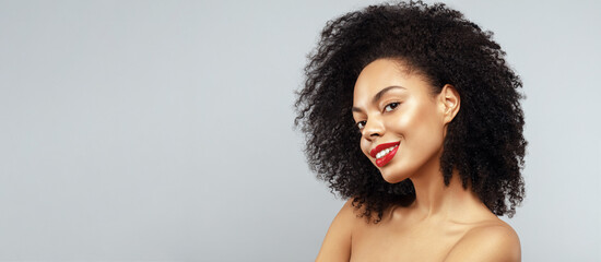 Beauty portrait of African American model with curly afro hair and red lips make up is smiling and...