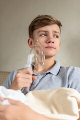 Sick teen boy with an inhaler. Unhealthy child doing inhalation at home, she use nebulizer and inhaler for the treatment, sitting on the couch at home. Asthma inhaler, nebulizer steam, flu or cold