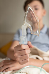 Sick teen boy with an inhaler. Unhealthy child doing inhalation at home, she use nebulizer and inhaler for the treatment, sitting on the couch at home. Asthma inhaler, nebulizer steam, flu or cold