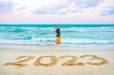 New Year 2023 on the sand, happy woman with hands up jumping on the beach