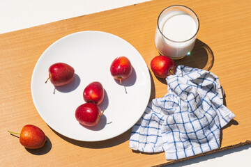 Fresh ripe mini apple or crabapple with fresh milk in a transparent glass on wooden cutting board in direct sunlight.