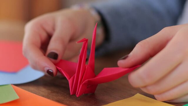 Origami crane. Japanese paper craft. Young woman's hands finish it.