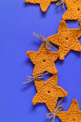 Christmas garland made of yellow crochet star on a blue background. Christmas and New year concept. Handmade decor.