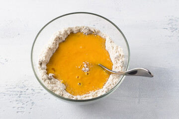 Glass bowl with oat flour and pumpkin puree, cooking pumpkin pancakes with oatmeal or cooking other dishes on a light gray background. Preparation healthy homemade vegan food