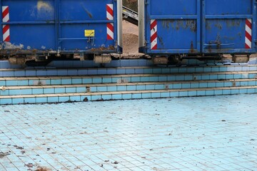 Zwei alte blaue rollende Container aus Metall stehen über blauem Schwimmbecken ohne Wasser am...