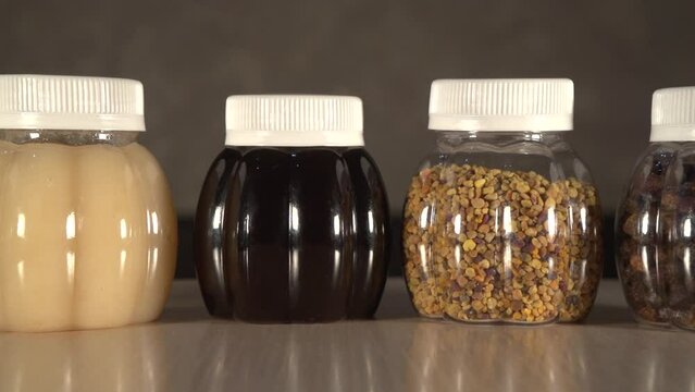 Close up panning to three plastic jars of different kinds honey, perga and pollen on table with out of focus background. Light honey is Linden, dark honey is taiga, transparent honey is acacia