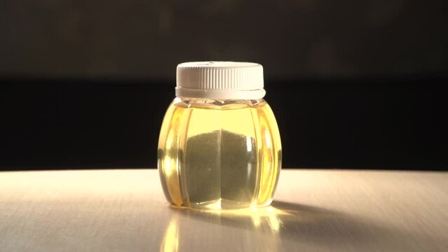 Close up plastic jar of acacia honey on table with out of focus dark background when light source is moving around. Jar with white cap