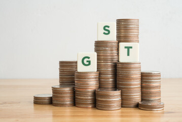 GST green letters word on stacks coins with white wall background copy space. Goods and services...