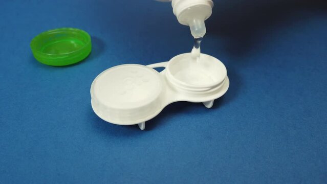 Filling contact lens case with solution on blue background