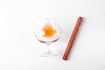 Cognac in a glass and a cigar. Strong alcoholic drink on white table