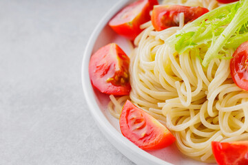 Cooked spaghetti with fresh cherry tomatoes on a white plate. Spaghetti pasta with vegetables on a gray background. Top view. Copy space
