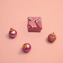Christmas present box and beautiful decorative balls on baby pink background. Flat lay cocnept.