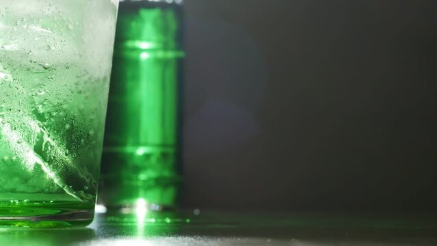 A glass and a bottle with a green drink on the table with direct sunlight and glare. Dolly shot green glass filled with fizzy drink and the walls are covered with drops. copy space