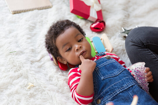 Close up of African American little boy lying on floor and playing with decoration items for Christmas tree at home. Christmas holiday celebration, Merry Christmas