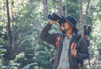 Young male hiker with backpack holding binoculars looking on green forest