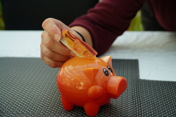 Eine Hand steckt einen 10 Euro Schein in ein Sparschwein