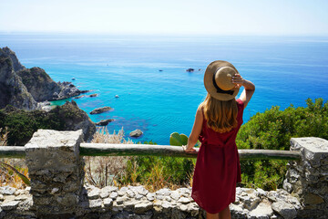 Beautiful young woman with hat looking at stunning panoramic view of Capo Vaticano on Coast of the...