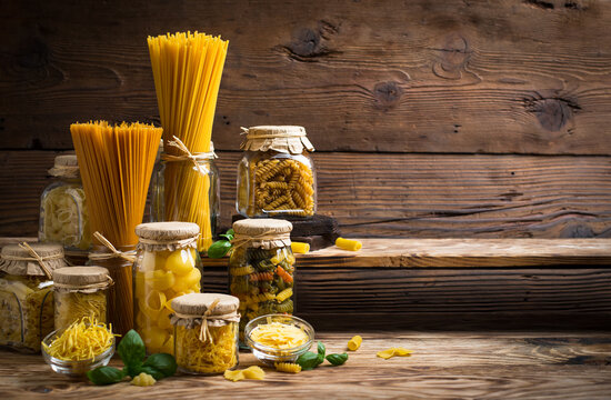 Variety of raw, uncooked pasta in the jars on the wooden table
