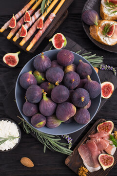 Appetizers with figs, prosciutto slices and cheese on the dark wooden background
