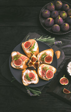 Sandwiches with ricotta cheese, sliced prosciutto and figs on the dark wooden background
