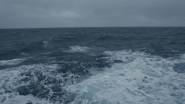 Storm at sea. Waves from ship. Wind breaks waves. White foam on wind. Side view along ship. Splashes.