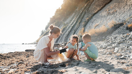 Little siblings helping mother to collect garbage on sea beach in plastic bag. Happy family activists collecting trash. Concept about environmental conservation pollution problems and responsibility.