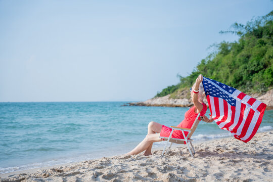 Senior couple relaxing and holding american flag at tropical beach.