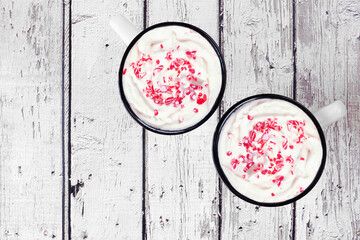 Two cups of Christmas hot chocolate with candy cane sprinkles. Top view on a white wood background.